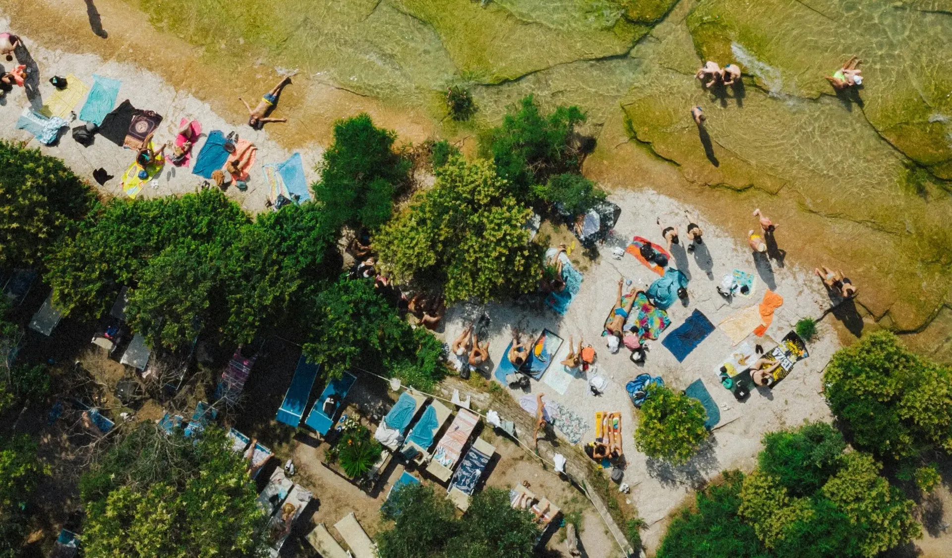 Aerial view of people sunbathing on towels along a river bank.