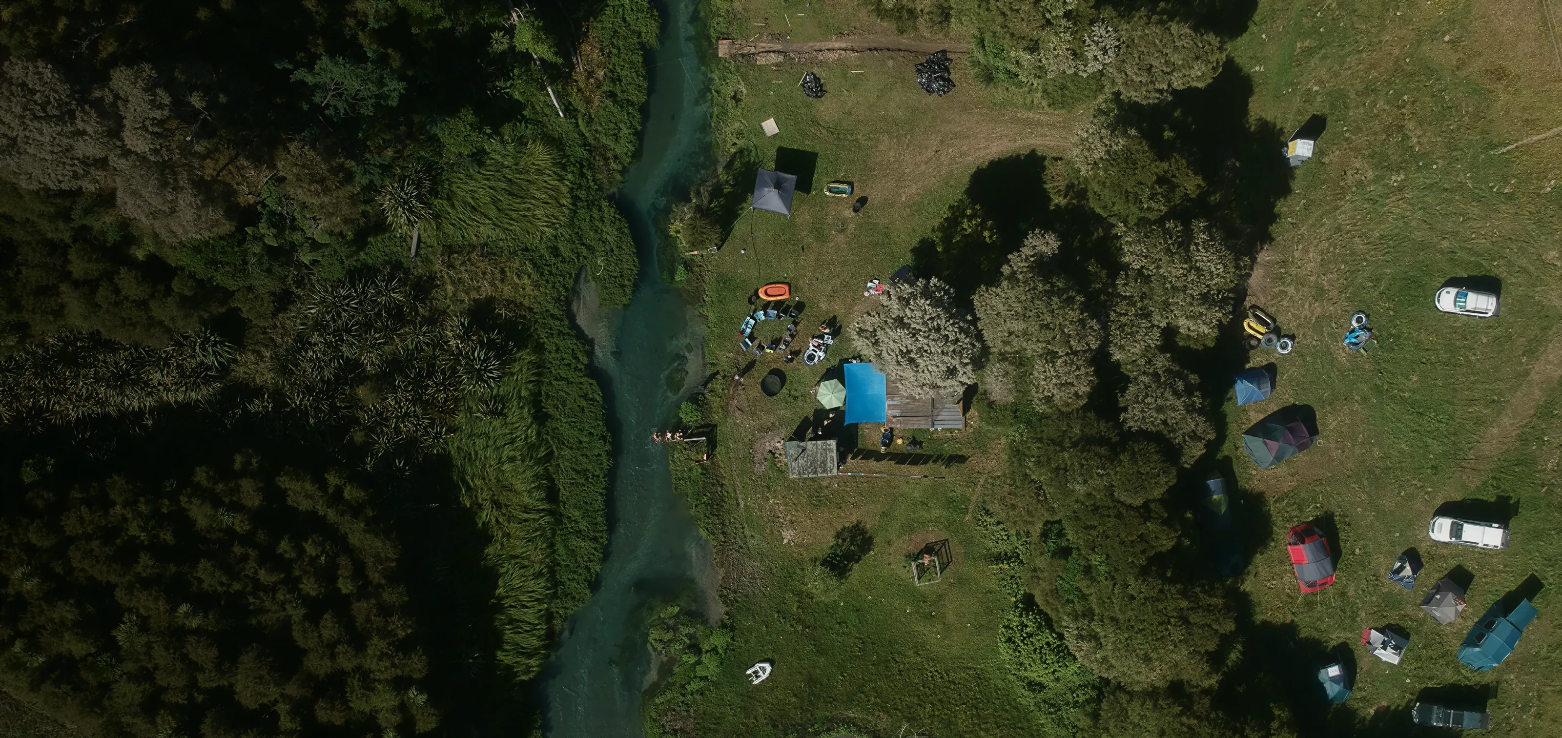 Aerial view of tents pitched in a meadow beside a winding river.
