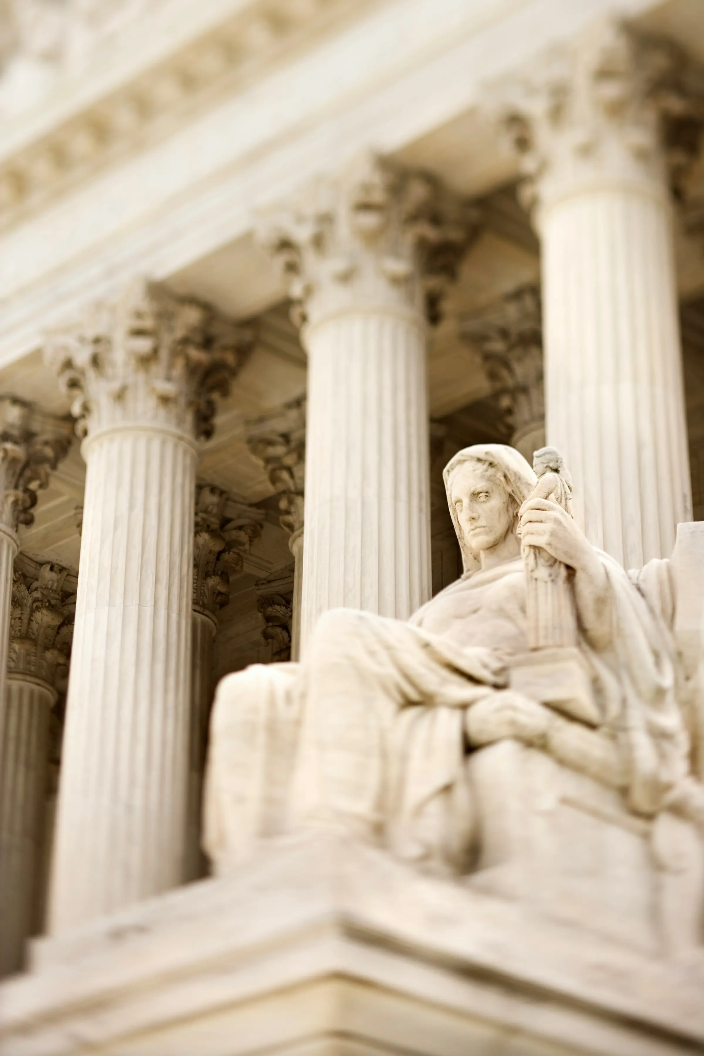 A marble statue seated between the columns of a courthouse.