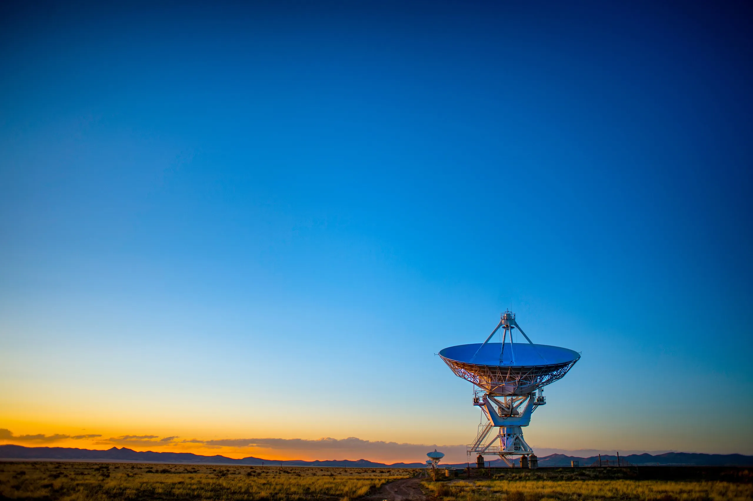 A radio telescope dish against a clear blue sky at dusk.