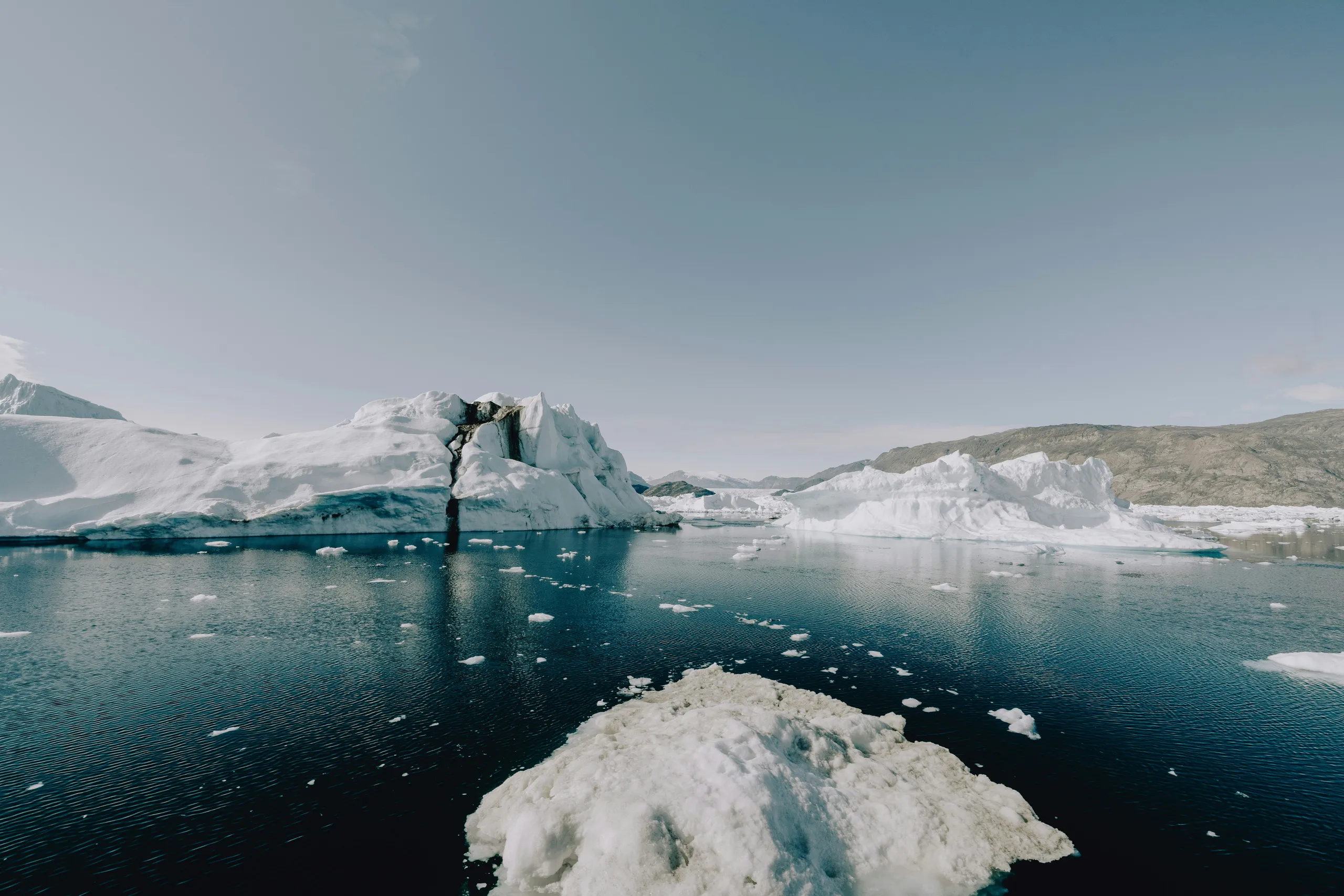 Icebergs floating on dark water beneath a pale sky.